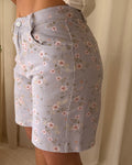 Person wearing a light blue floral skirt with a neutral background