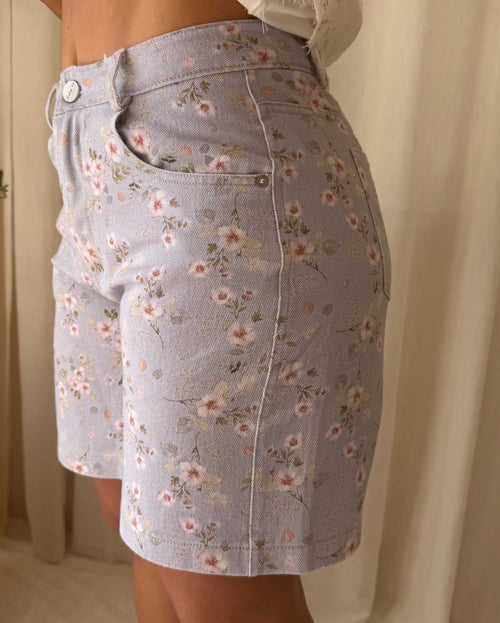 Person wearing a light blue floral skirt with a neutral background